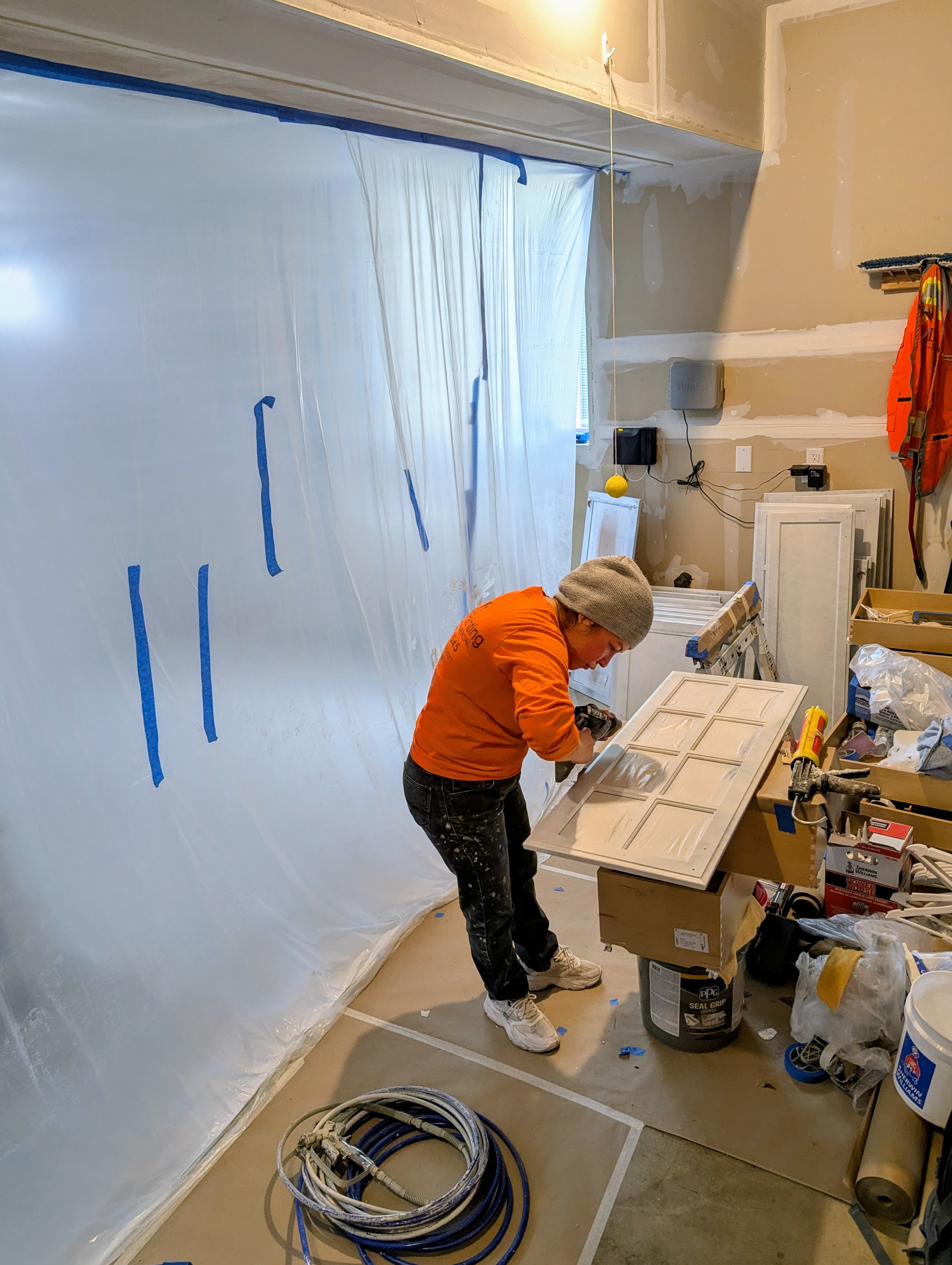 Painter prepping a cabinet door inside a sealed cabinet painting workspace